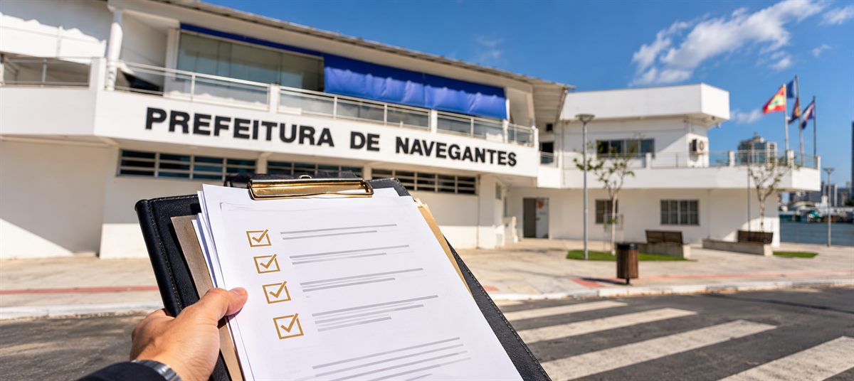 Prancheta com documentos de abertura de empresa diante da fachada da Prefeitura de Navegantes